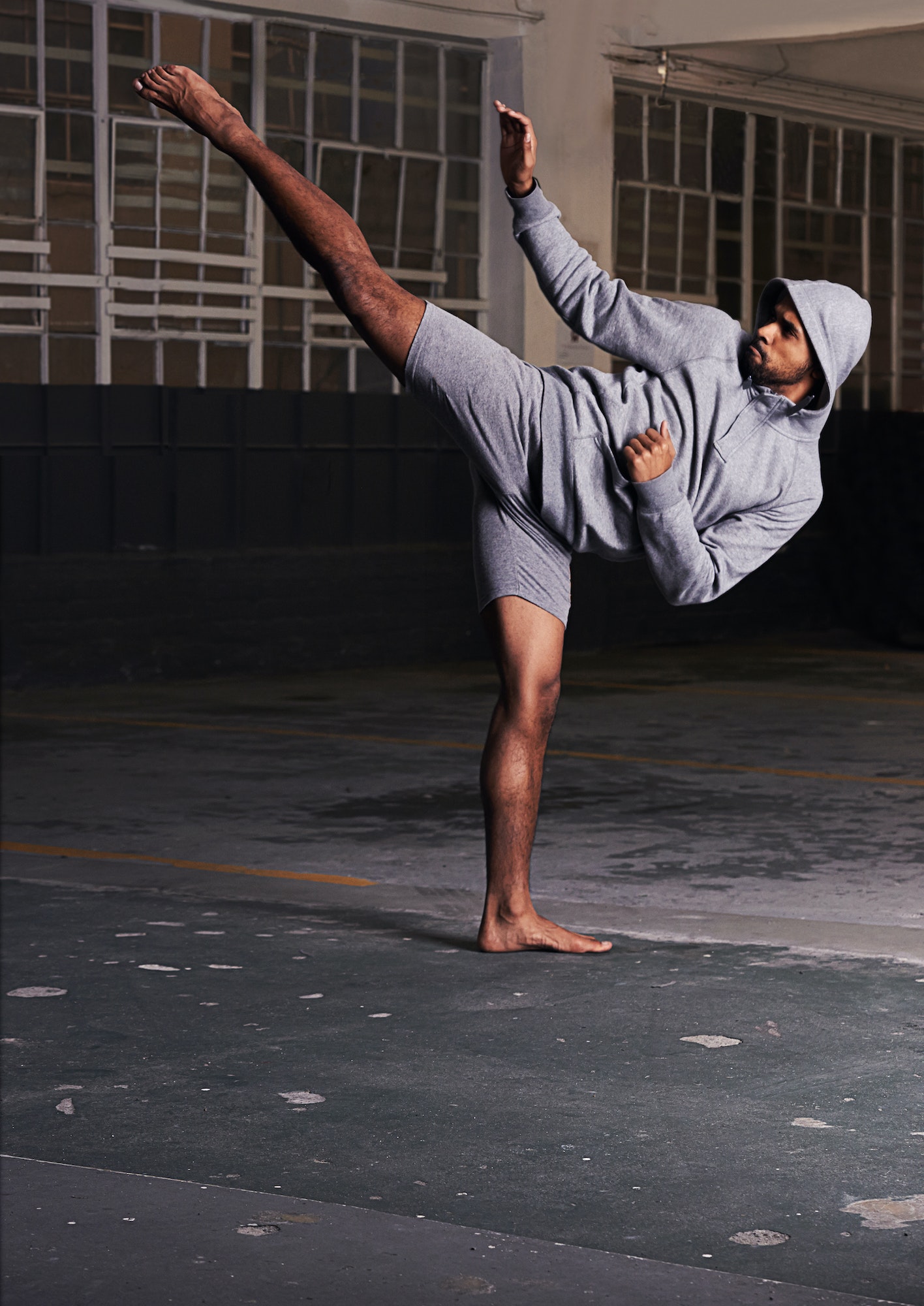 Shot of a barefoot young man in activewear doing martial arts in a parking lot