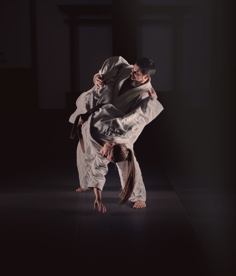 Young judo practitioners showing sweeping hip throw technique in black studio